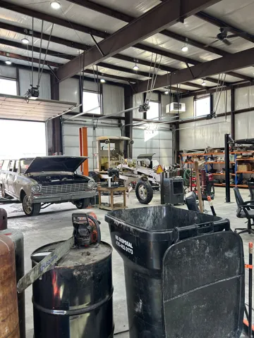 Large open-span warehouse space with exposed structural steel beams, multiple overhead garage doors, high ceilings with recessed lighting, integrated ceiling fans, and concrete flooring