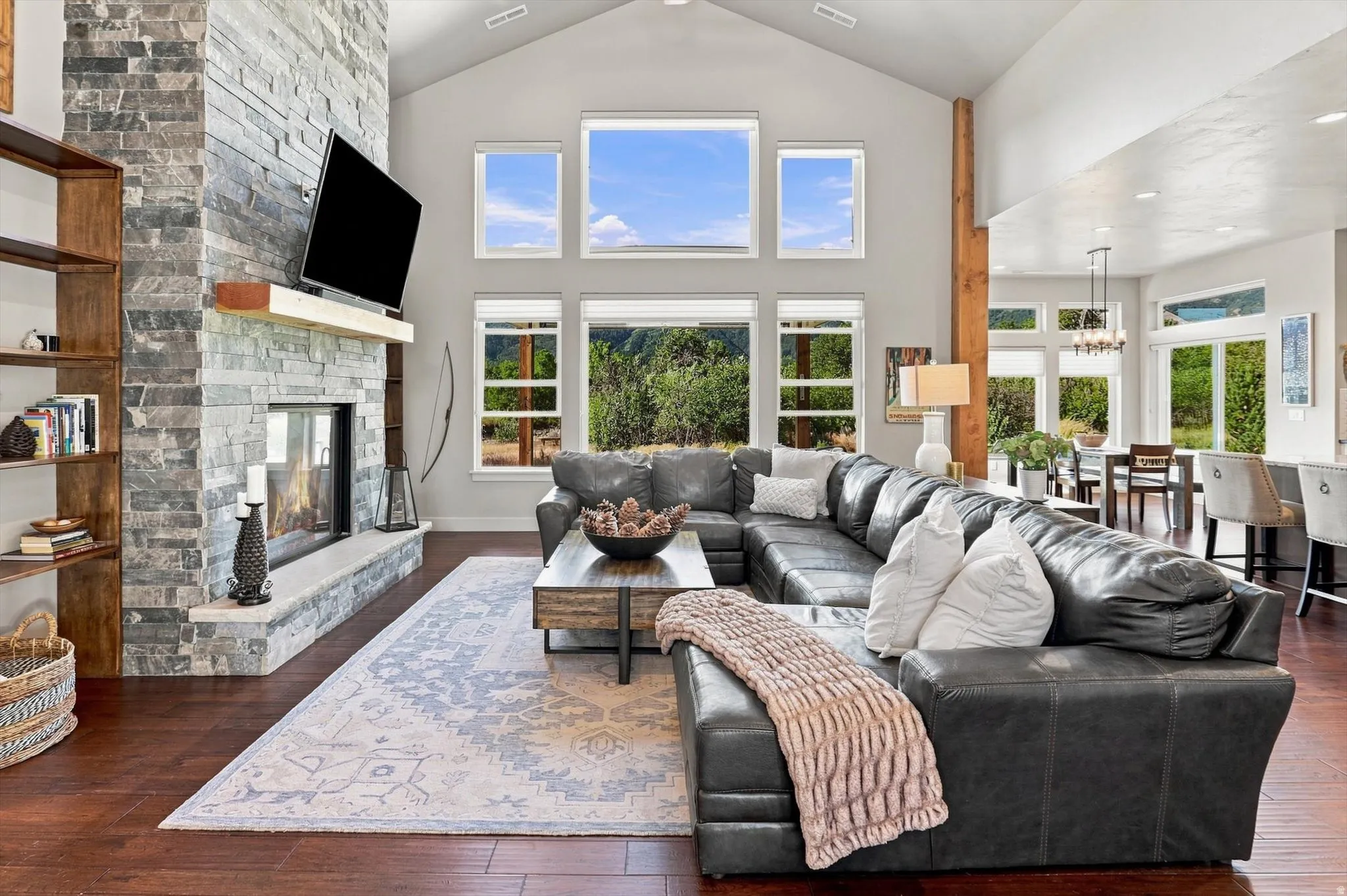 Vaulted ceiling, stone-clad fireplace with mantel, expansive window array, wood-finish flooring, and recessed lighting