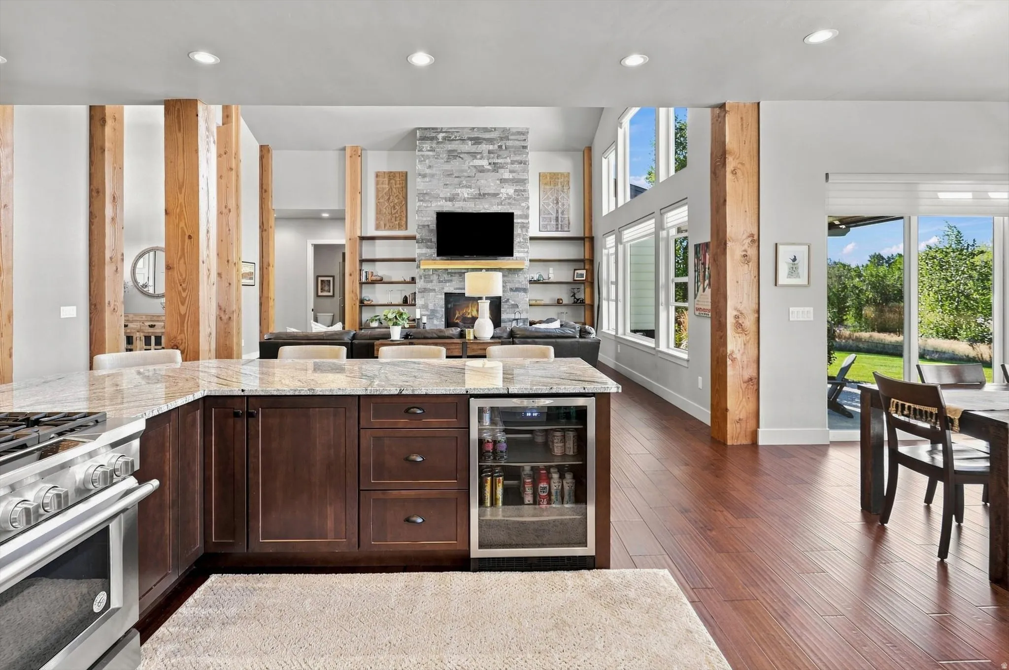 Kitchen island with stone countertop, built-in beverage cooler, stainless steel range, wood-finish flooring, and exposed wood beam accents