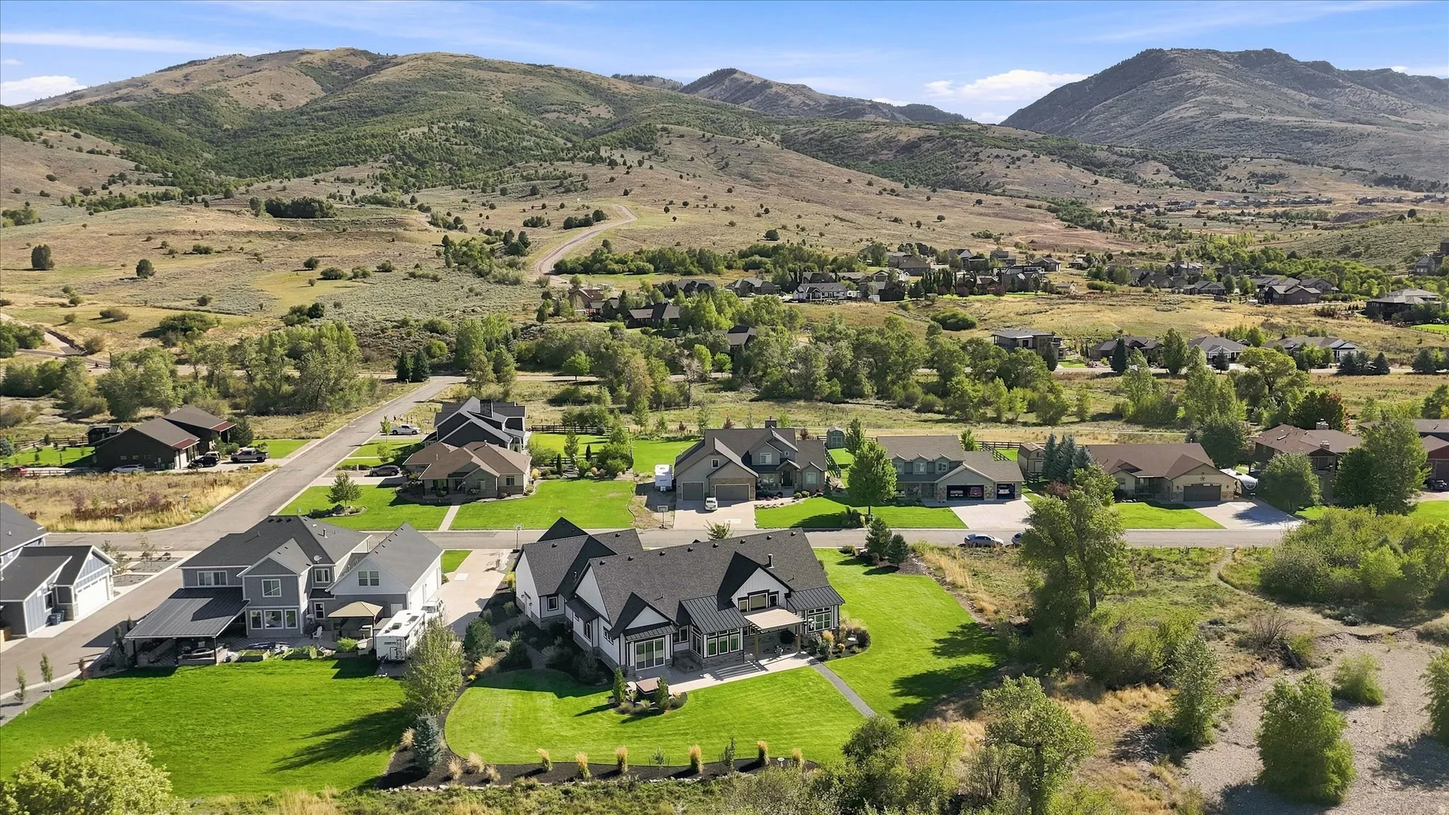 Expansive residential development with manicured lawns, mature trees, and mountainous terrain in the background