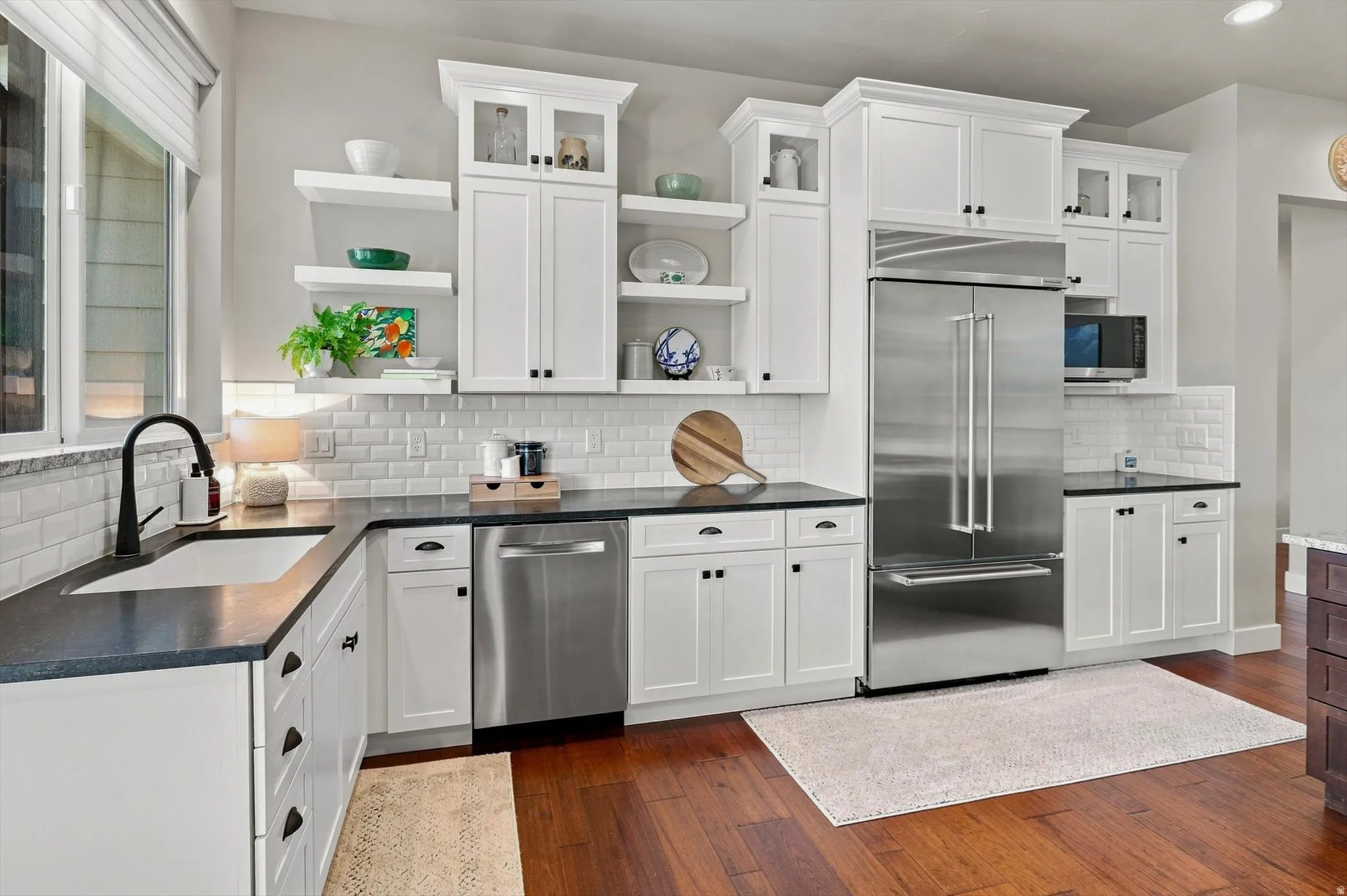 Kitchen featuring white cabinetry, subway tile backsplash, dark countertops, stainless steel appliances, and wood-finish flooring