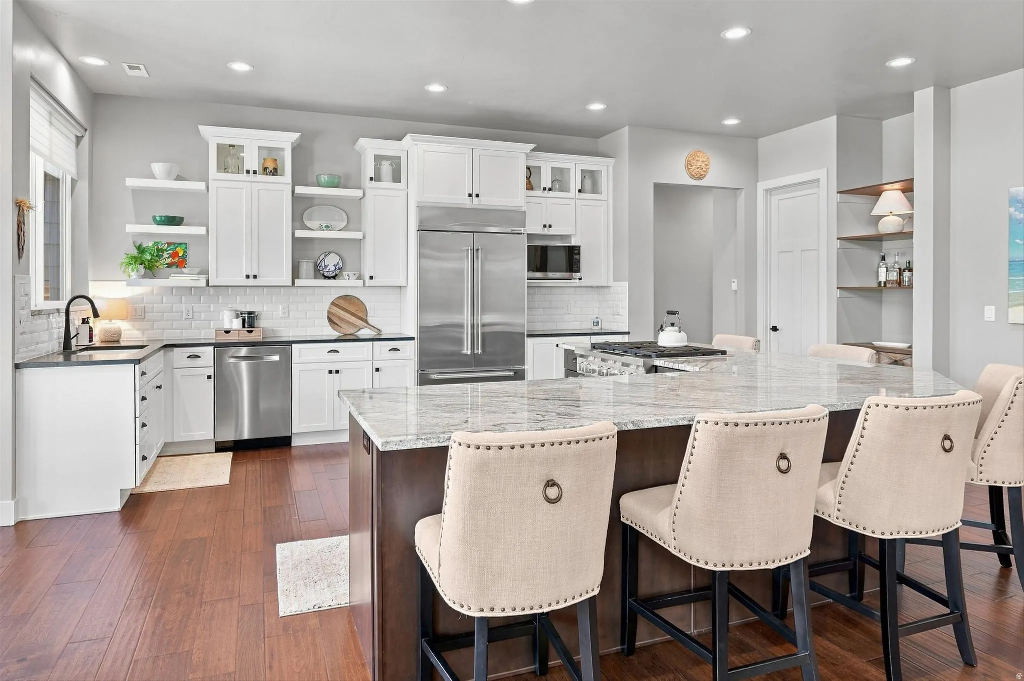 Kitchen featuring white cabinetry, subway tile backsplash, stainless steel appliances, a large island with a light-toned countertop, and wood-finish flooring