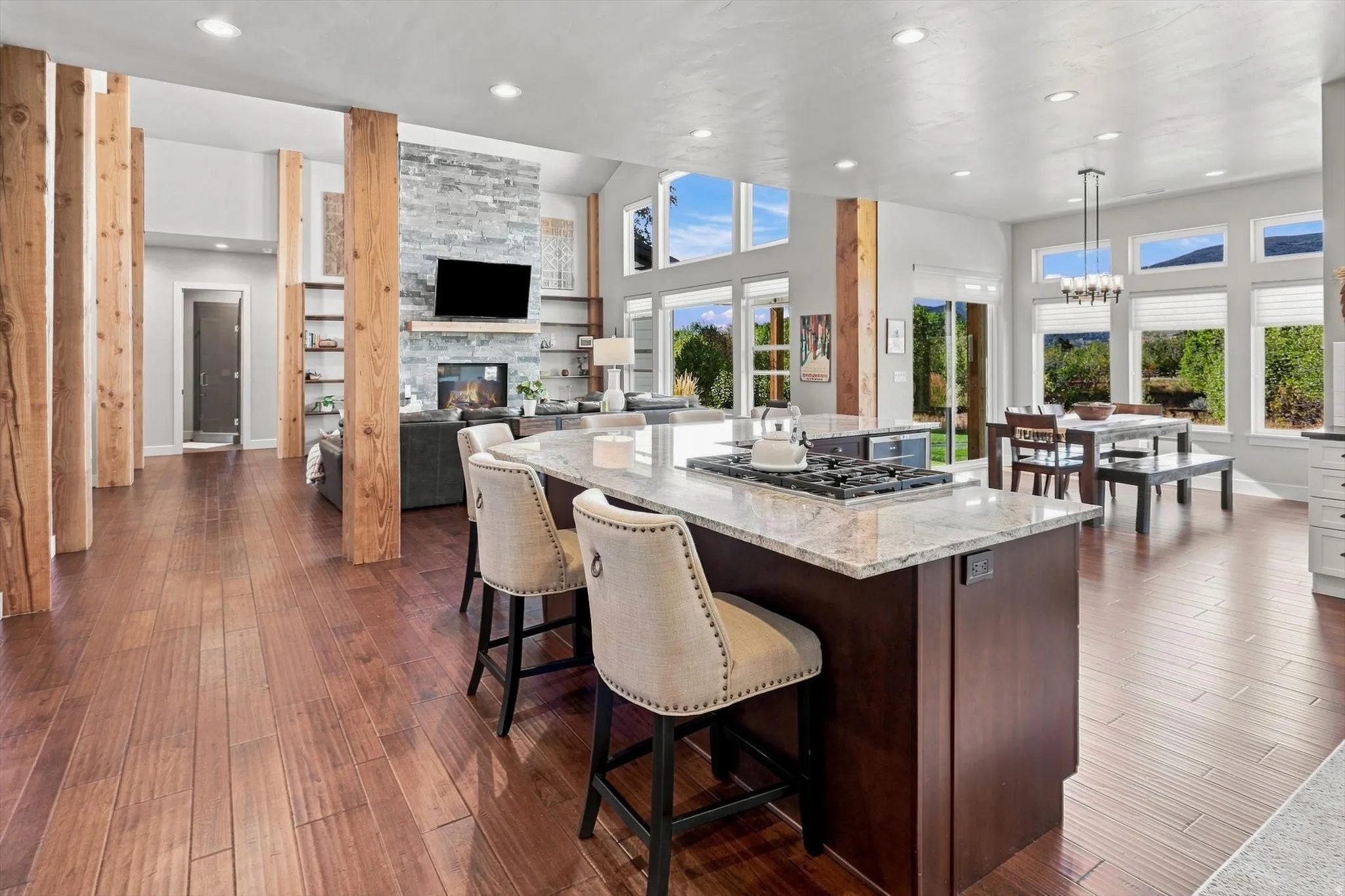 Open-concept living area with wood-finish flooring, a kitchen island featuring a gas cooktop and stone countertop, and a fireplace with stone surround