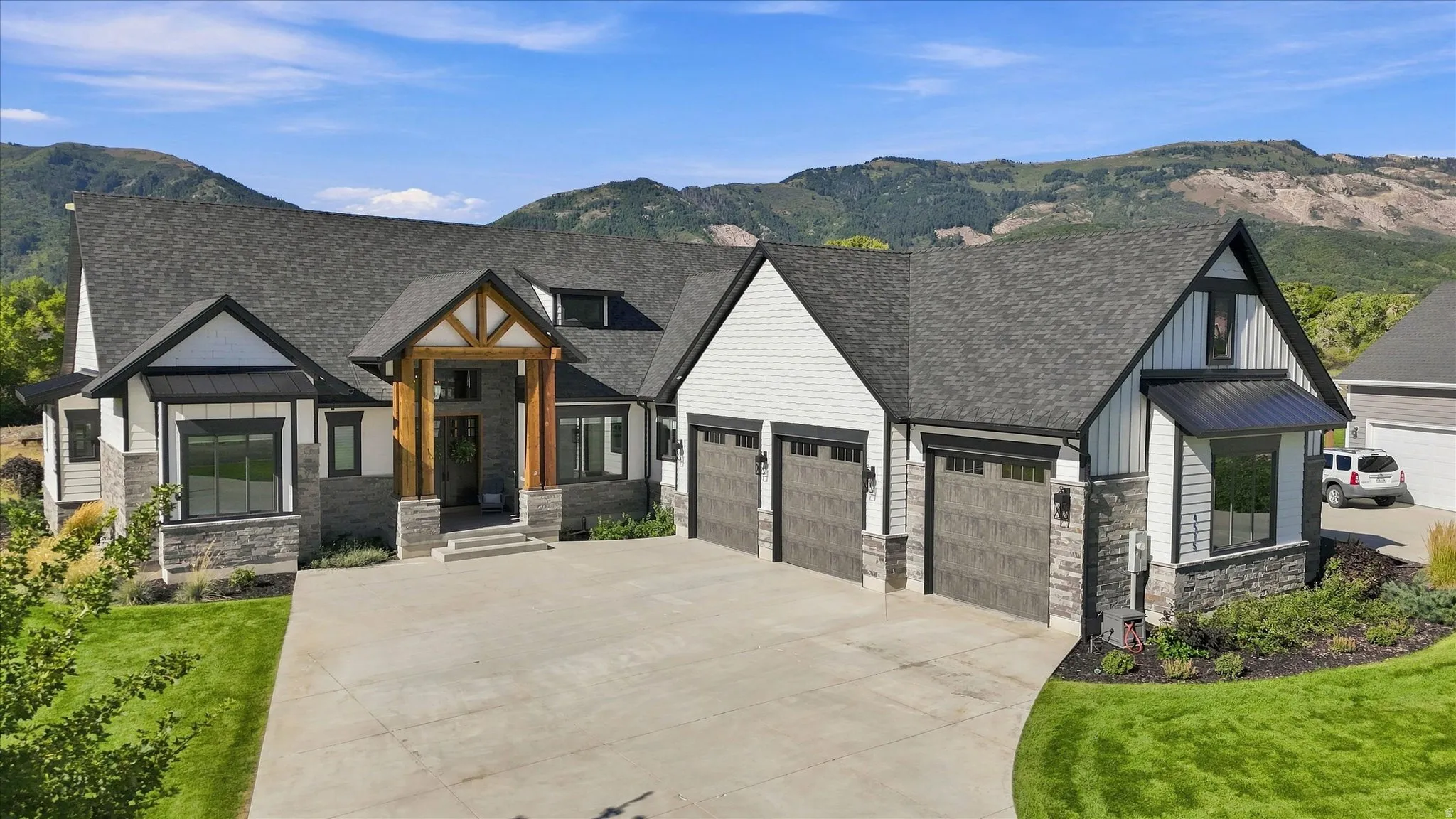 Exterior featuring stone and siding finishes, a multi-car garage, a covered entry with timber detailing, a paved driveway, and a mountain backdrop