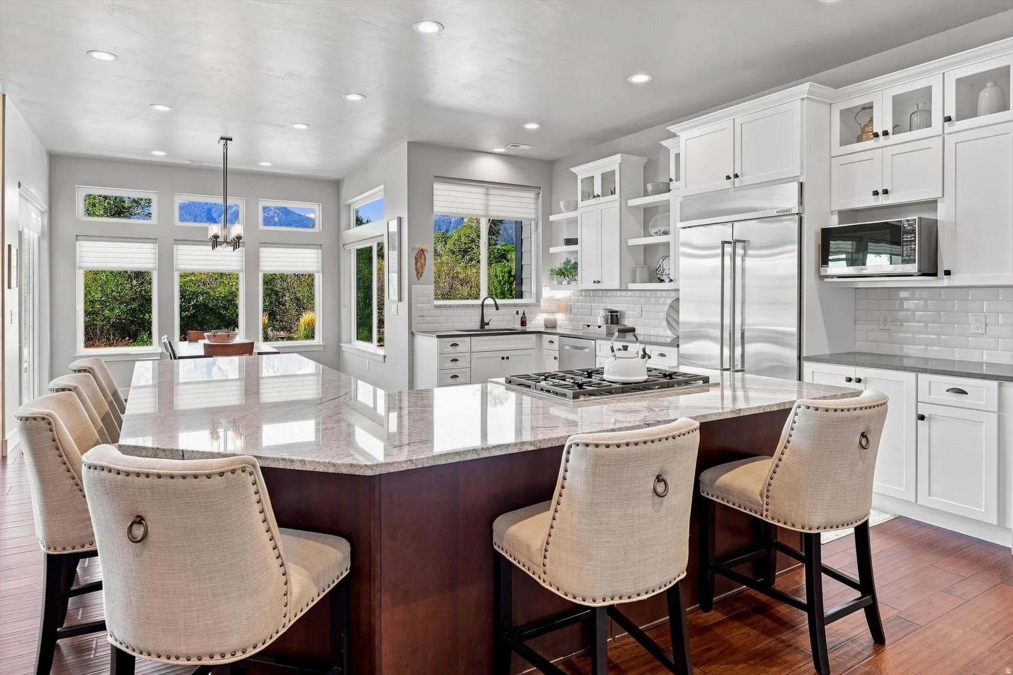 Gourmet kitchen with a large central island, white cabinetry, integrated stainless steel appliances, and wood-finish flooring