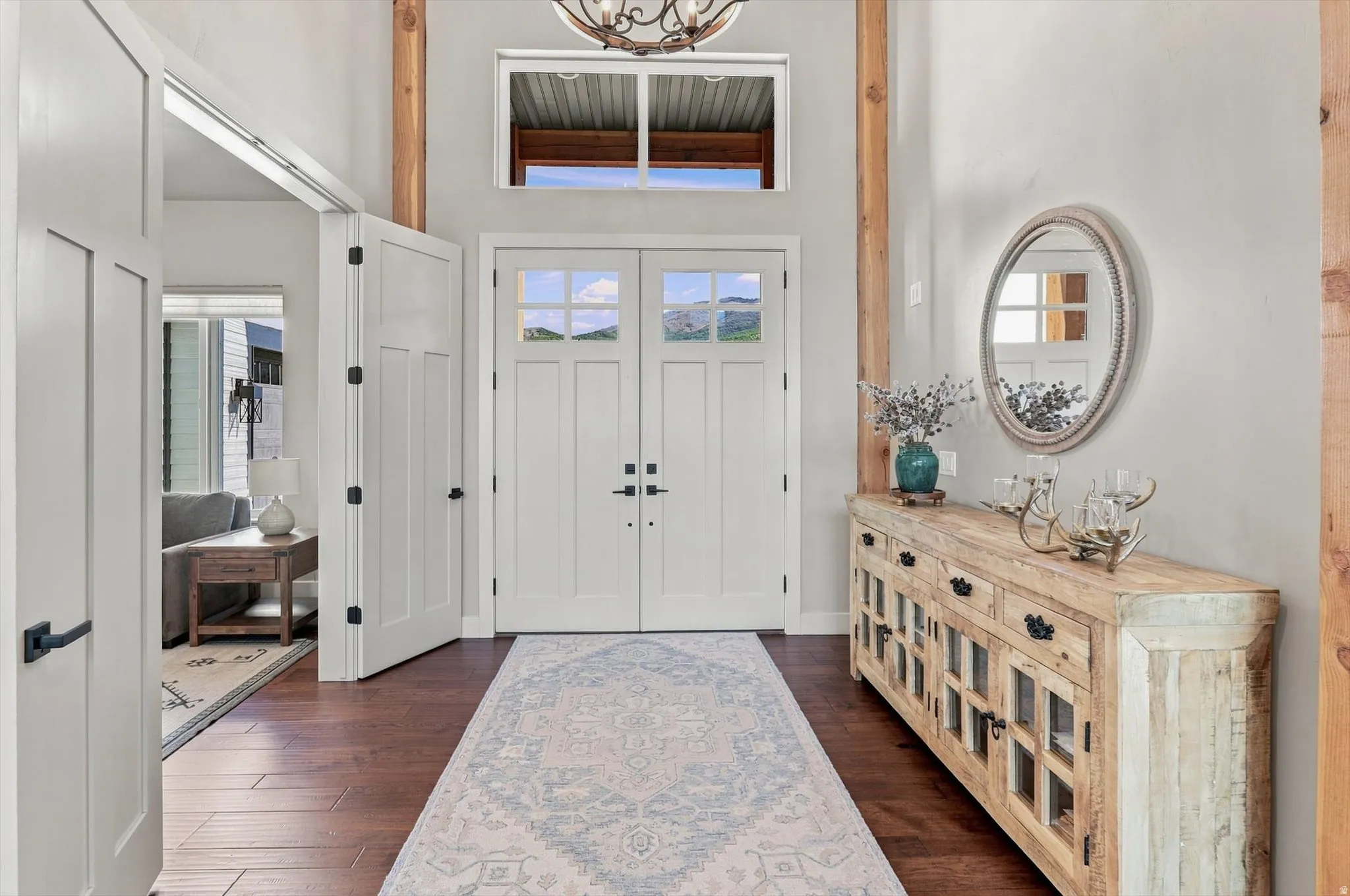 Double entry doors with glass panes, wood-finish flooring, a decorative transom window, and prominent exposed wooden beams