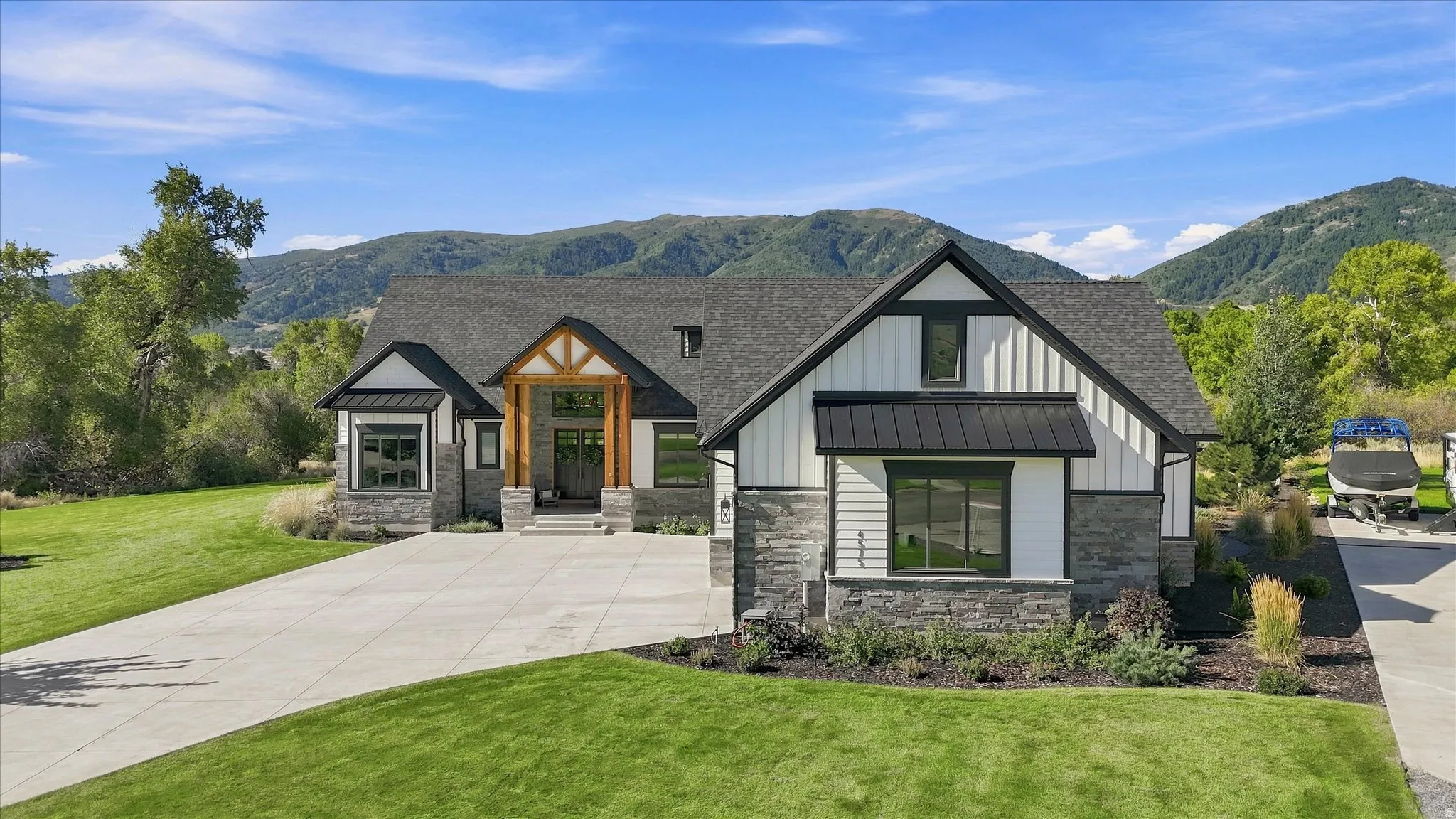 Modern craftsman-style exterior featuring stone and vertical siding, a deep gray shingle roof, and a prominent timber-framed entry