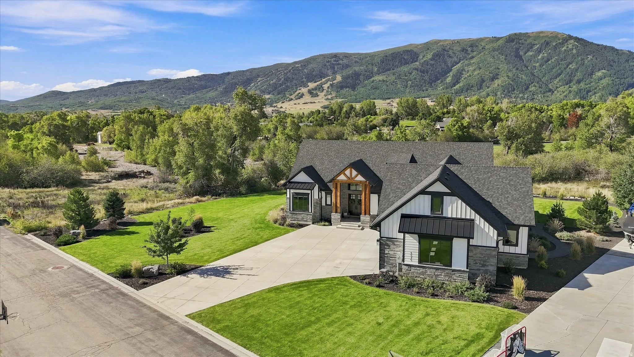 Contemporary exterior with stone and siding accents, prominent gables, a wide driveway, and a manicured lawn