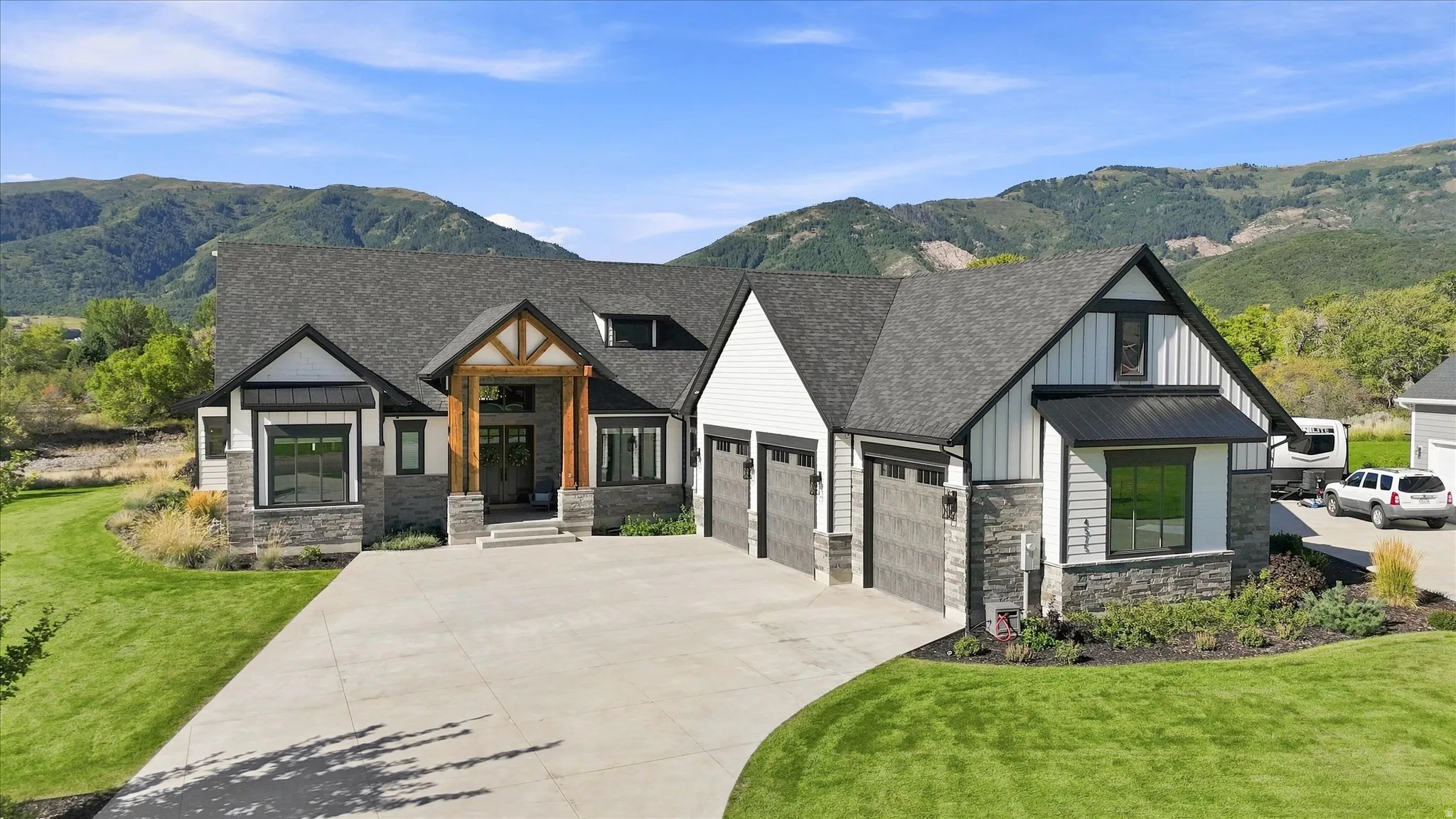 Modern mountain-style residence featuring a prominent timber-frame entry, stone and siding exterior, multi-car garage, and a concrete driveway