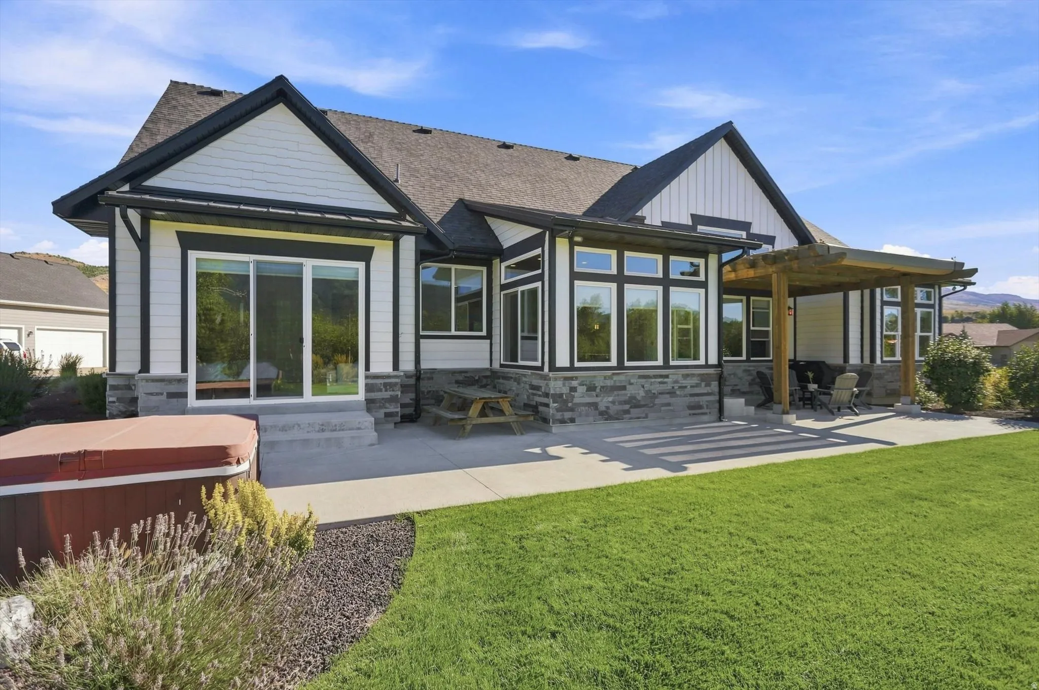 Expansive rear patio with a wood pergola, integrated landscaping, and a manicured lawn