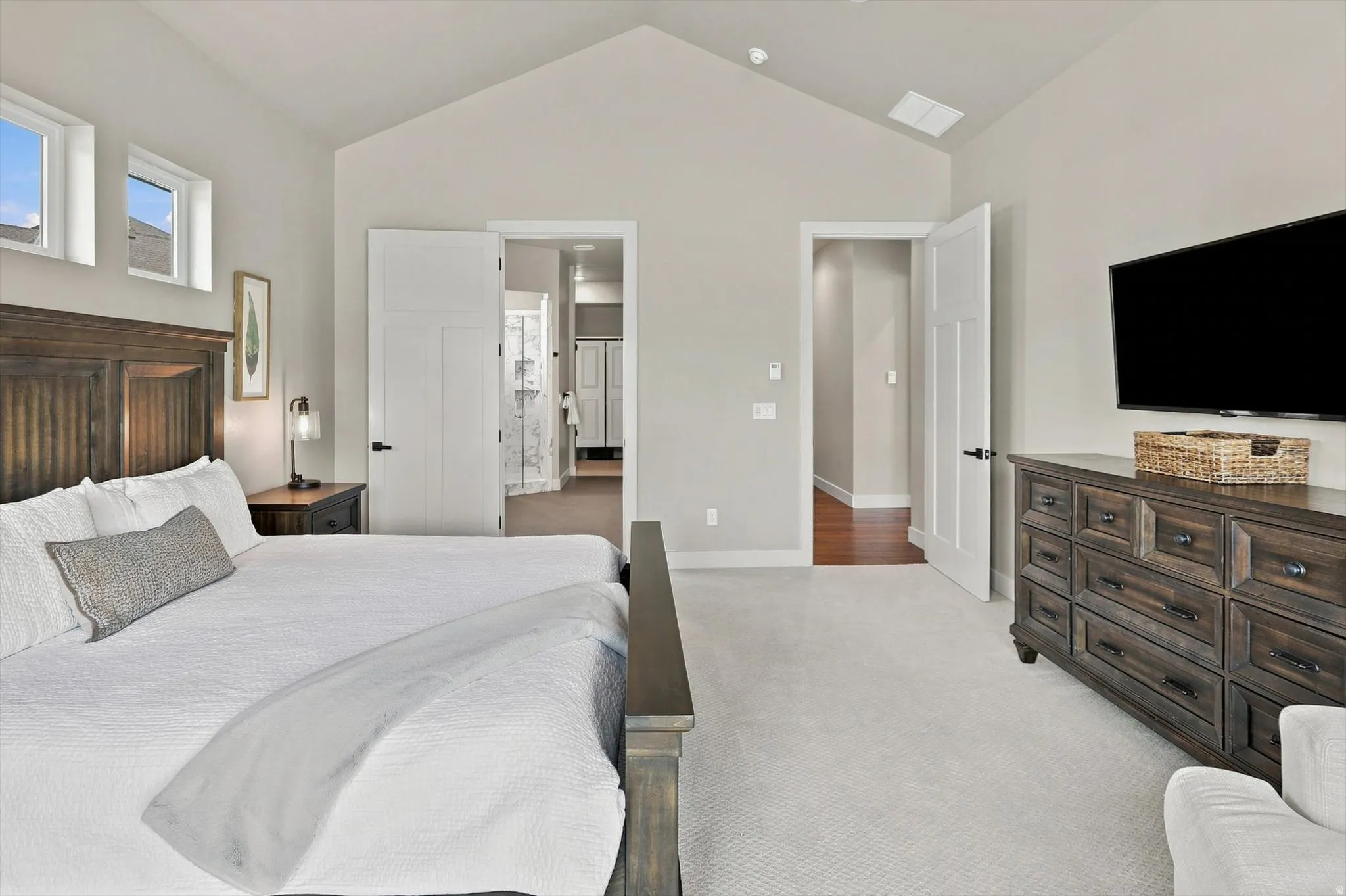 Vaulted ceiling, two transom windows, light neutral wall color, white paneled doors, and soft carpeting