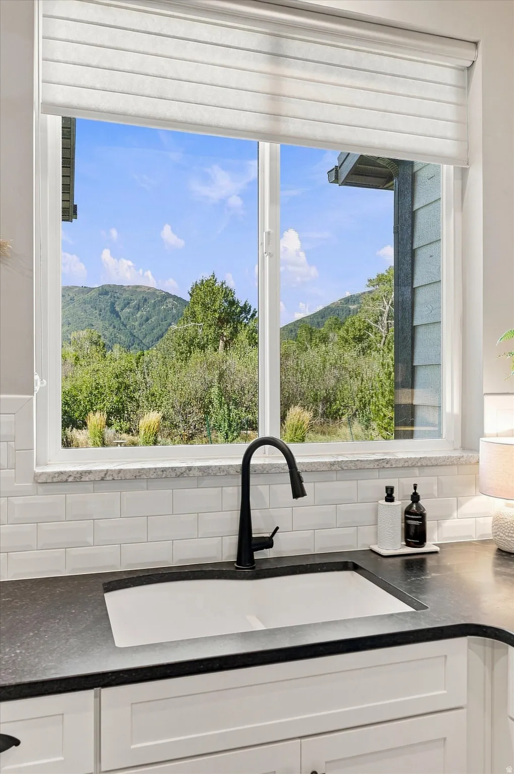 White kitchen cabinets, subway tile backsplash, dark countertop, single-basin sink, and a matte black gooseneck faucet