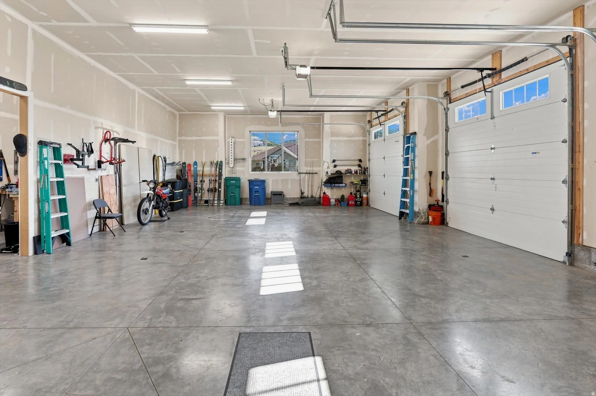 Spacious garage featuring a concrete floor, two white overhead doors with windows, and fluorescent lighting