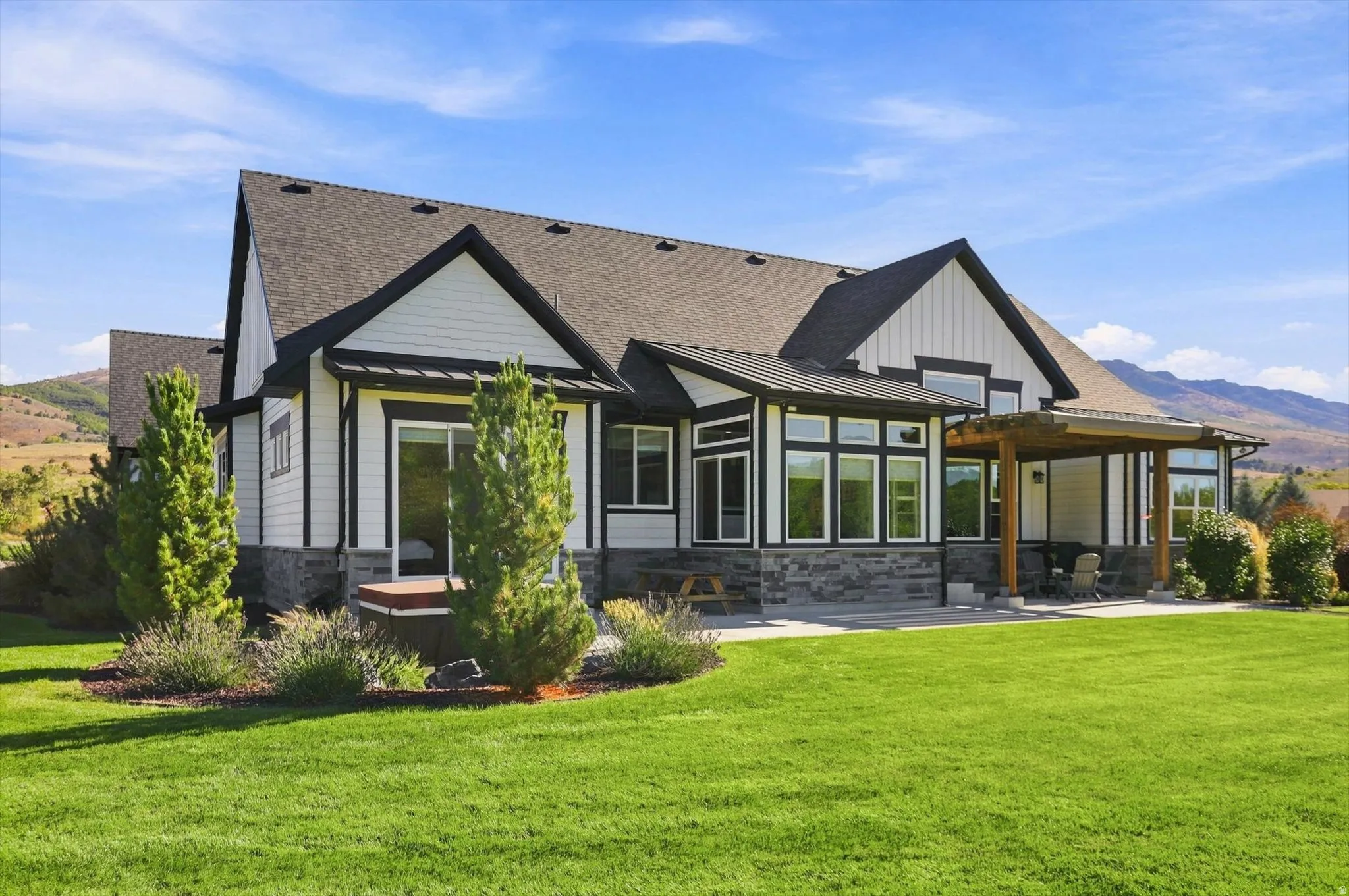 Exterior showcasing white siding, dark trim, a covered patio with a wood pergola, expansive green lawn, and stone detailing