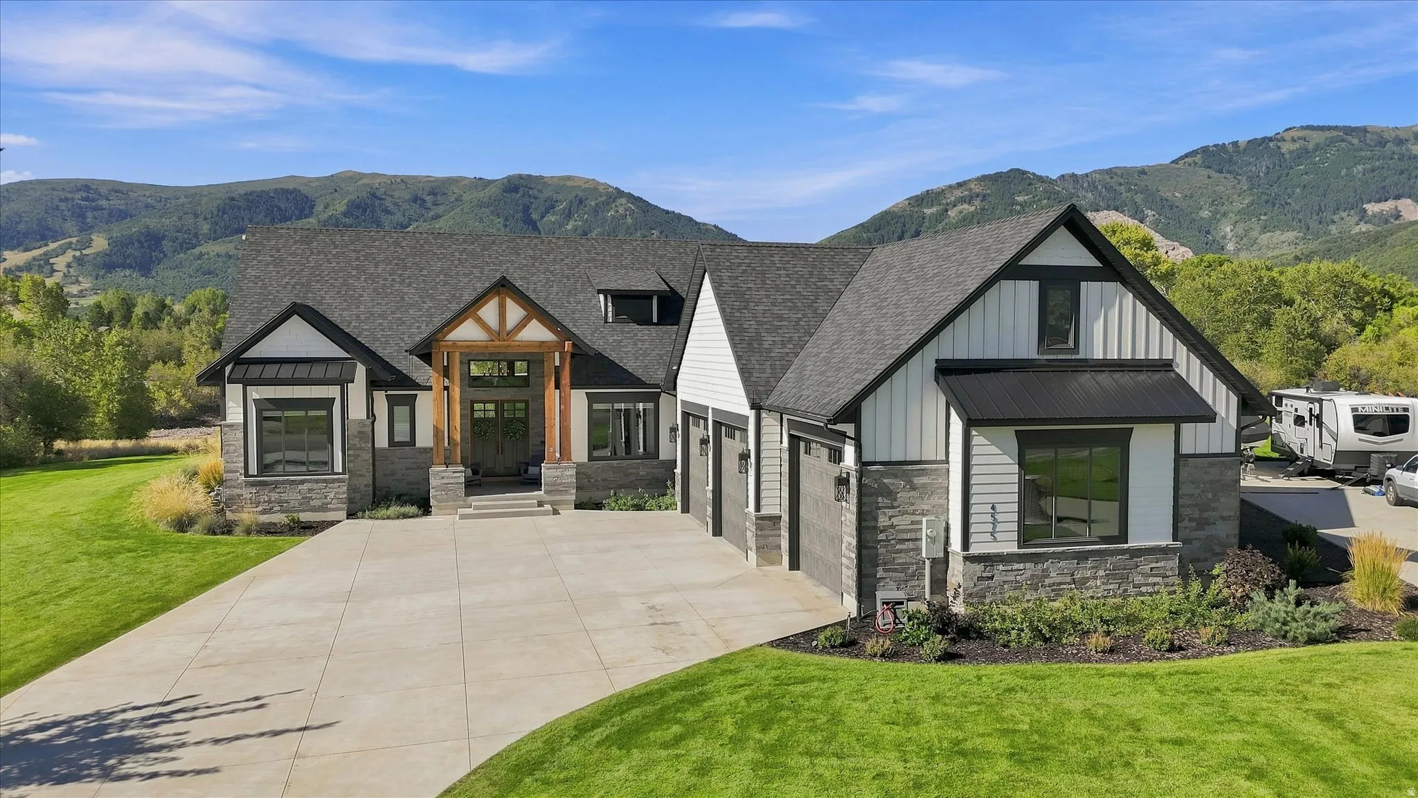 Craftsman-style exterior with stone and vertical siding accents, a prominent covered entry with wood beams, a concrete driveway, a two-car garage, and landscaped grounds