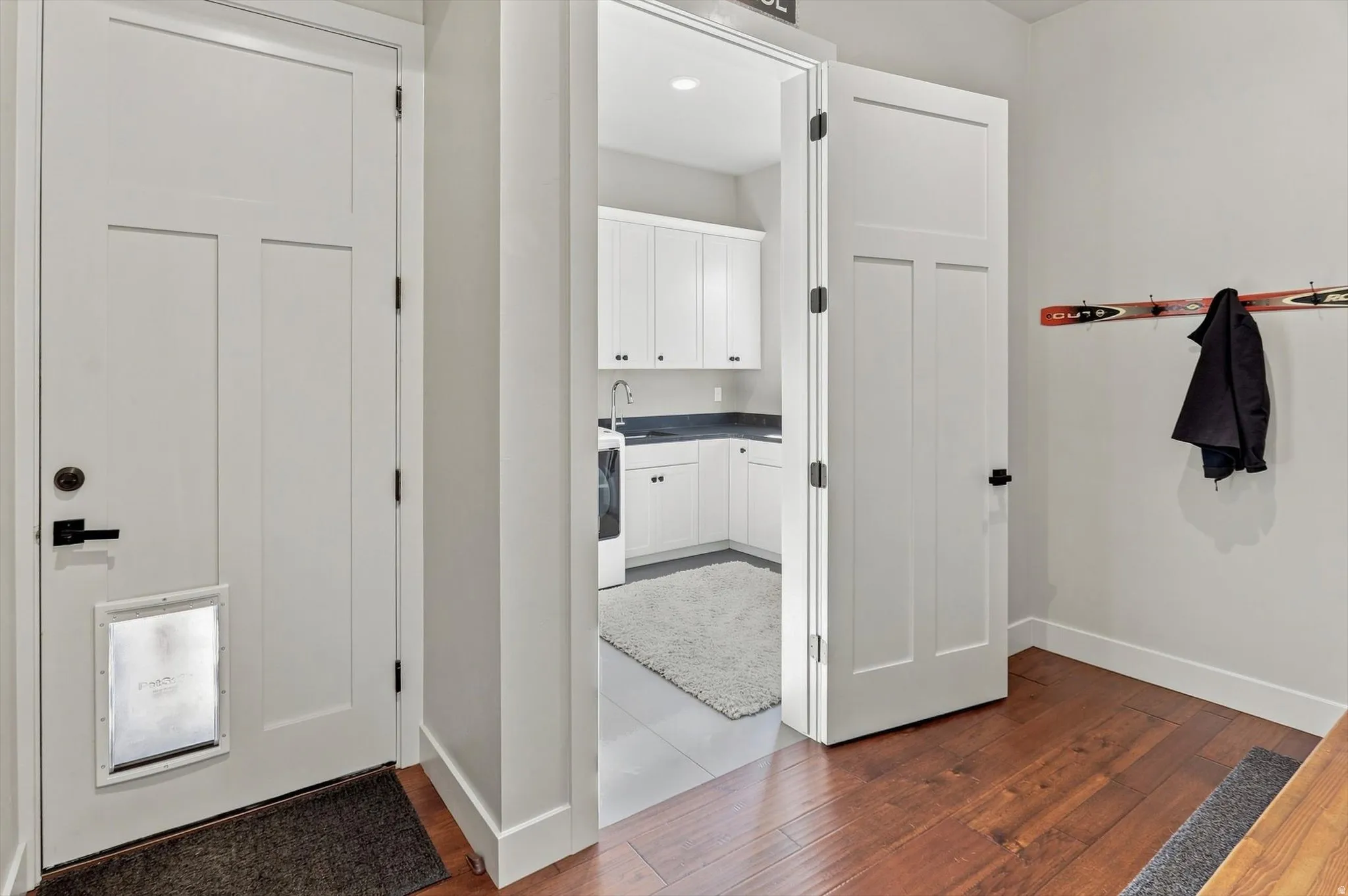 Hardwood-style flooring in entry area, white shaker-style cabinetry with dark countertops, recessed lighting, and a utility sink