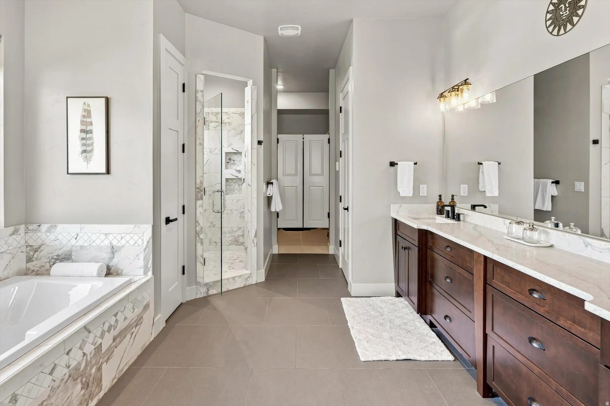 Spacious bathroom featuring a built-in soaking tub with marble surround, a glass-enclosed shower, dual vanity with wood cabinetry and stone countertops, and tile flooring