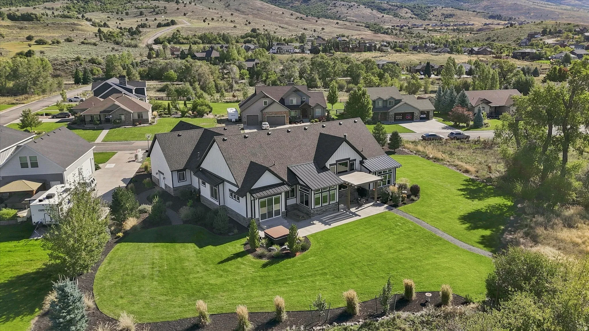 Expansive green lawn, dark shingle roofing, white siding, stone accents, and covered porch