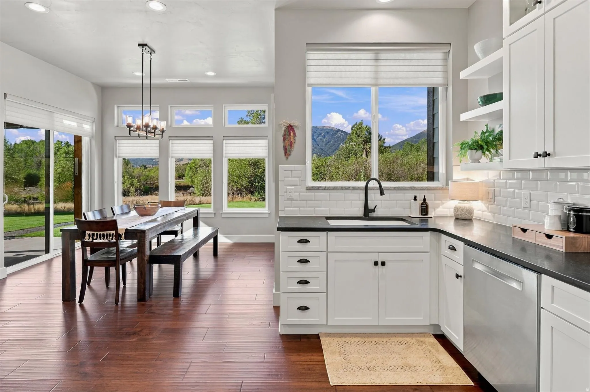 Open-concept kitchen and dining area featuring wood-finish flooring, white cabinetry, dark countertops, and a subway tile backsplash