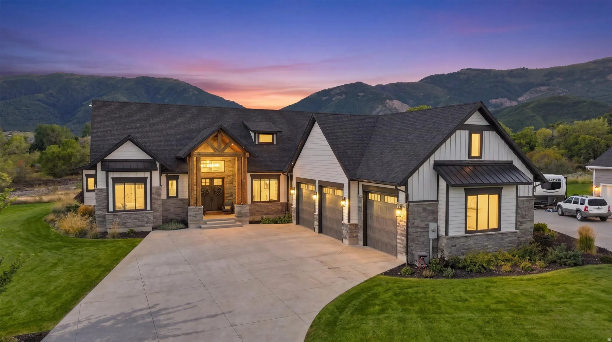 Modern-farmhouse exterior with stone and vertical siding accents, prominent dark-pitched roof, wood-beam entryway, and a large concrete driveway