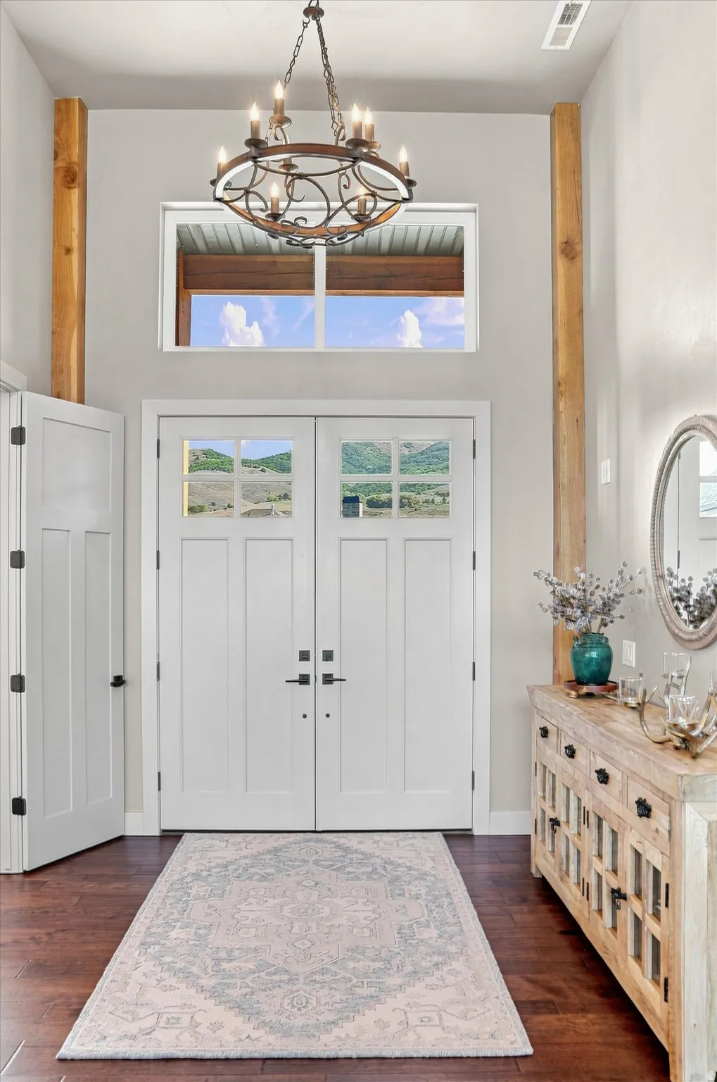 Double entry doors with glass panels, wood-finish flooring, a decorative chandelier, and exposed wood beams