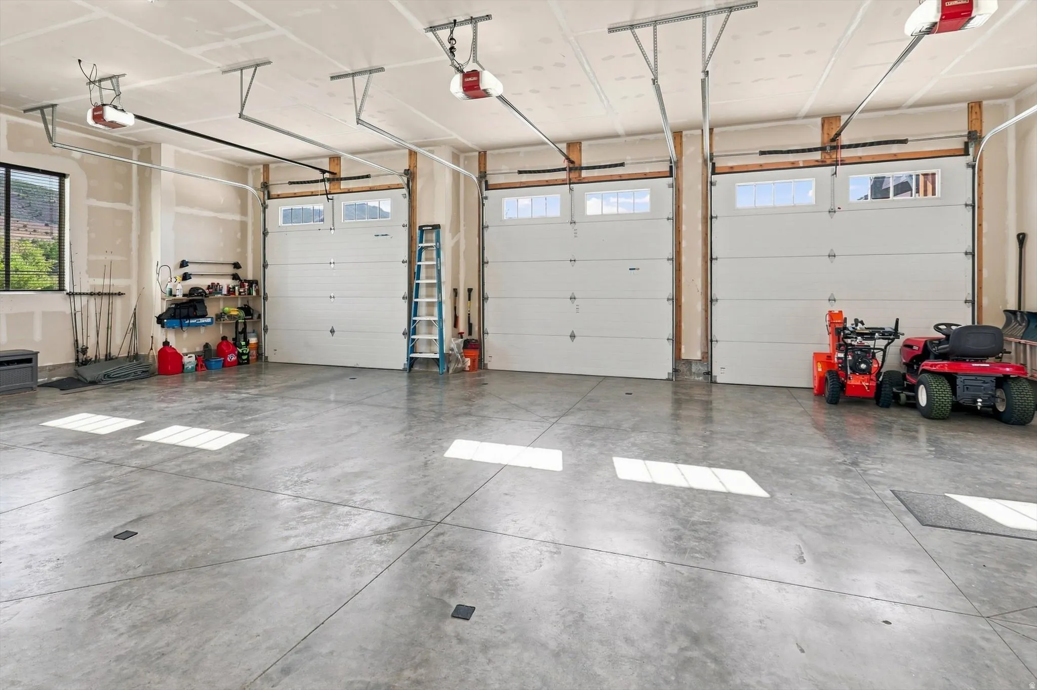 Concrete flooring, three garage doors with upper window panels, exposed wood framing, and a large window