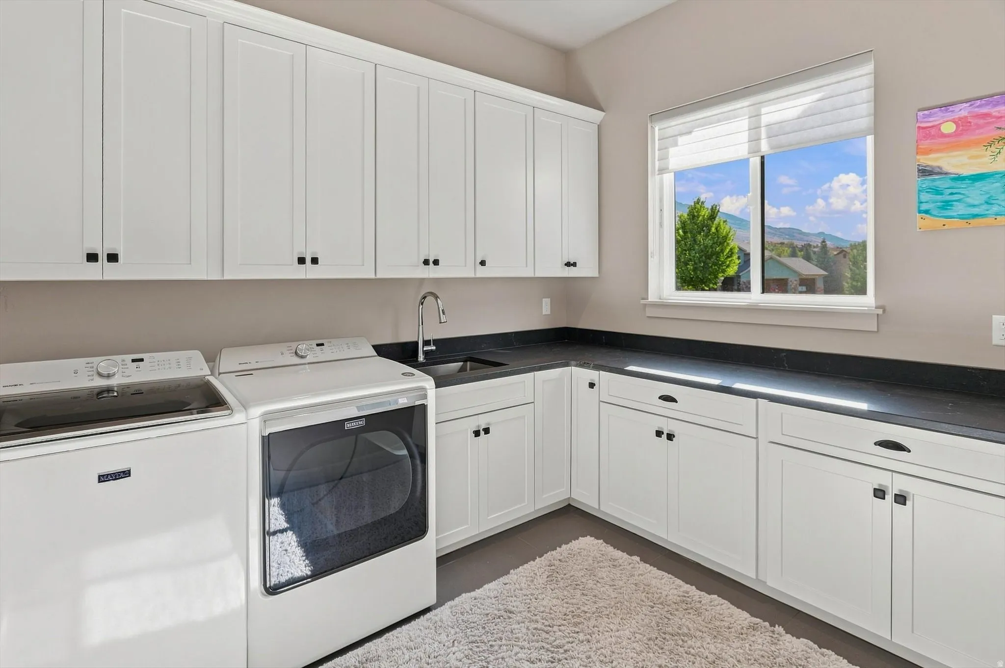 White shaker cabinetry with black hardware, dark countertops, and a window with mountain scenery