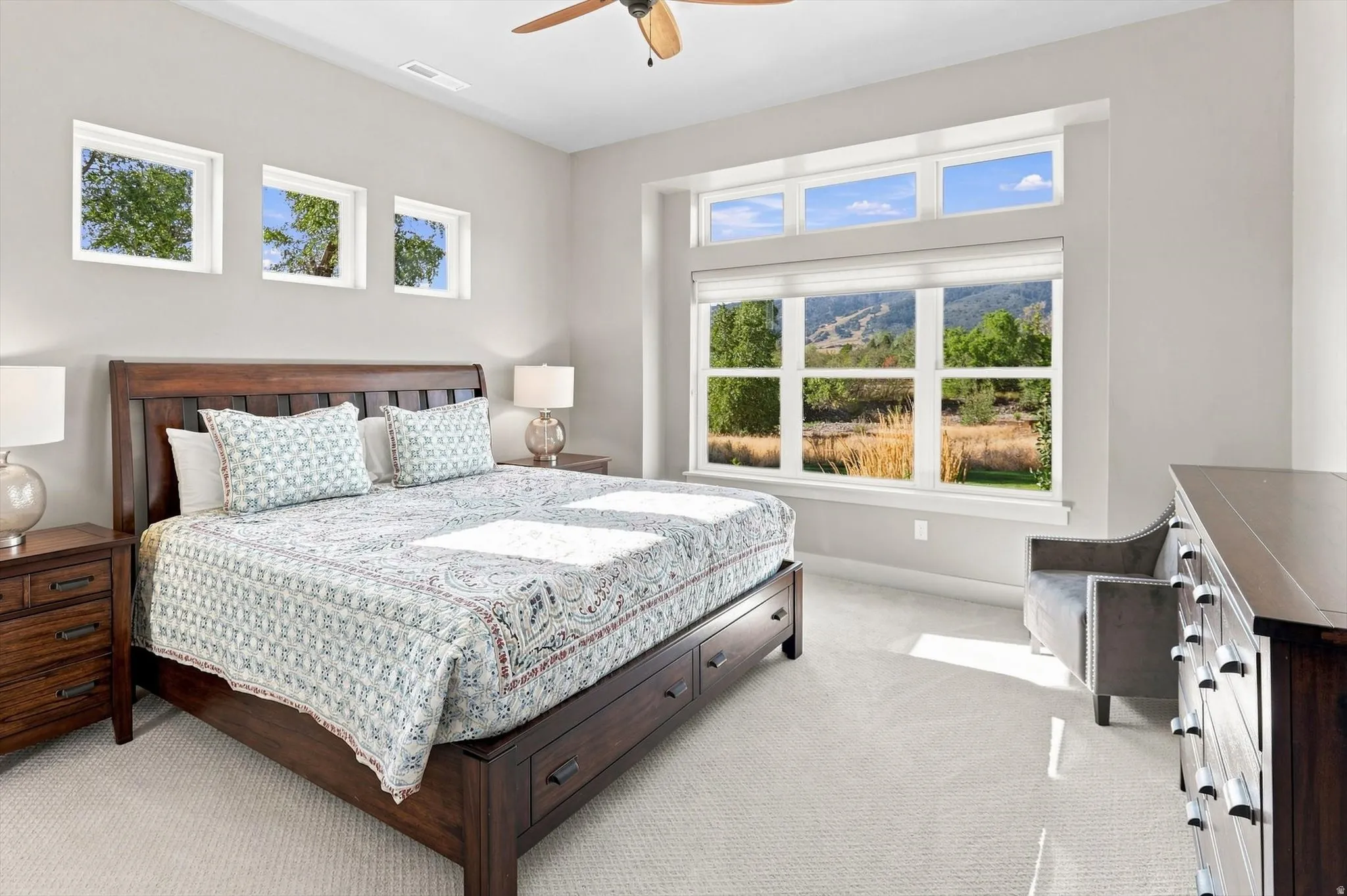 Expansive window arrangement, ceiling fan, carpeted flooring, and neutral wall tones