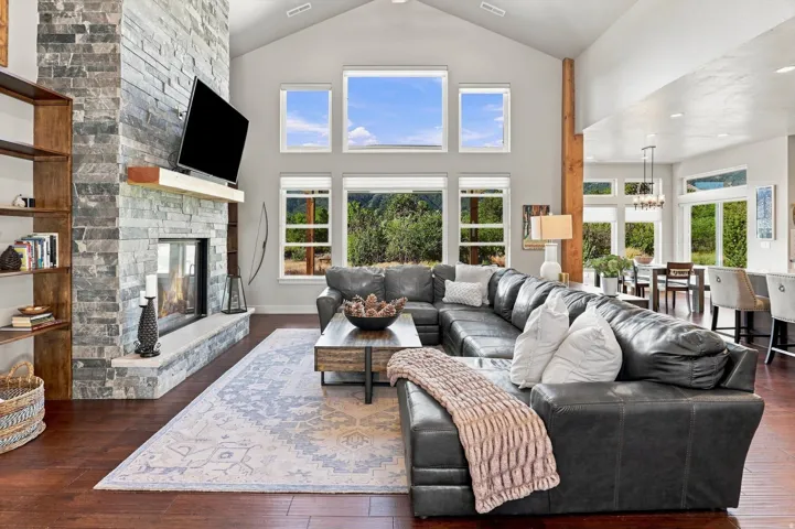 Vaulted ceiling, stone-clad fireplace with mantel, expansive window array, wood-finish flooring, and recessed lighting