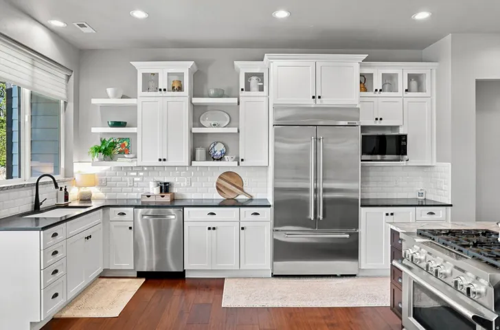 Bright kitchen featuring white cabinetry, dark countertops, stainless steel appliances, white subway tile backsplash, and wood-finish flooring