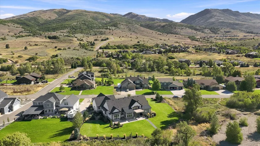 Expansive residential development with manicured lawns, mature trees, and mountainous terrain in the background