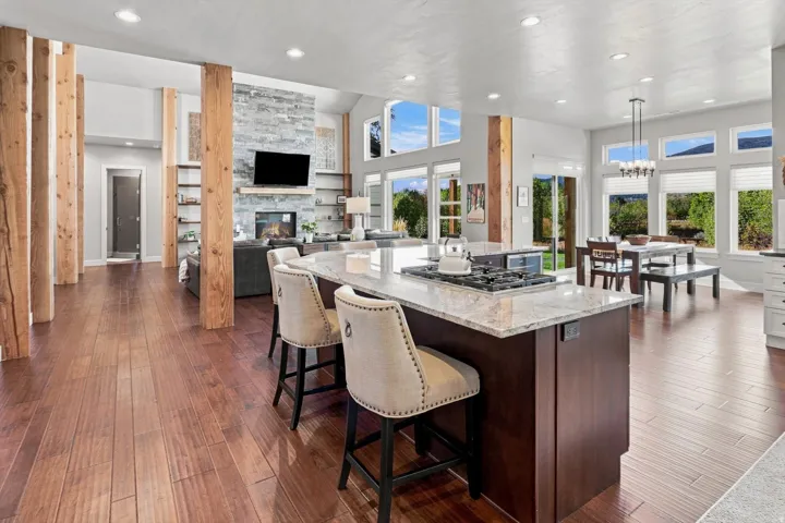 Open-concept living area with wood-finish flooring, a kitchen island featuring a gas cooktop and stone countertop, and a fireplace with stone surround