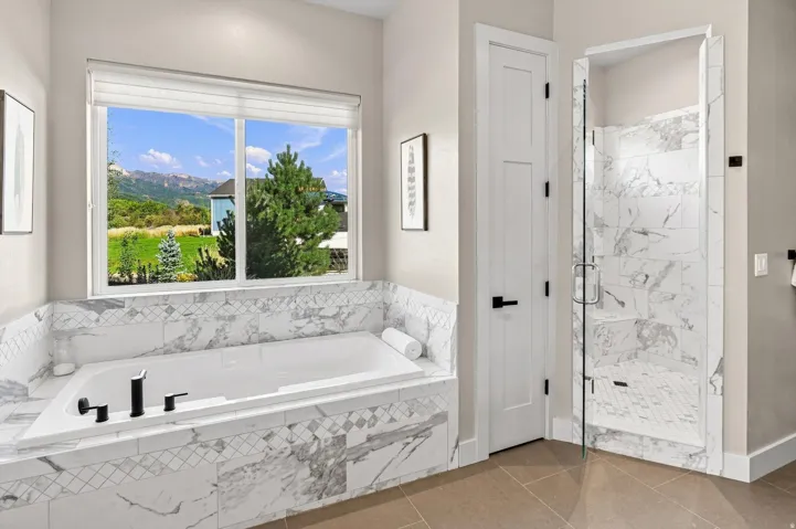 Built-in soaking tub with a tiled surround, separate glass-enclosed shower with tile, and large window