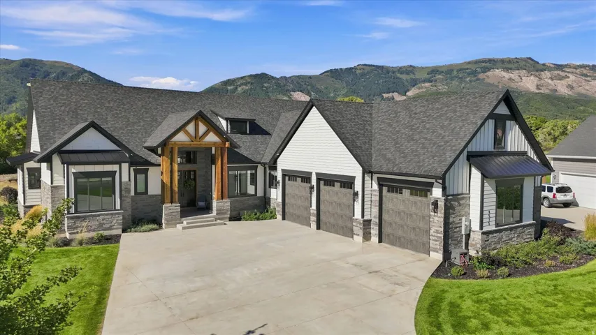 Exterior featuring stone and siding finishes, a multi-car garage, a covered entry with timber detailing, a paved driveway, and a mountain backdrop