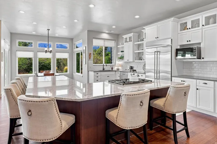 Gourmet kitchen with a large central island, white cabinetry, integrated stainless steel appliances, and wood-finish flooring