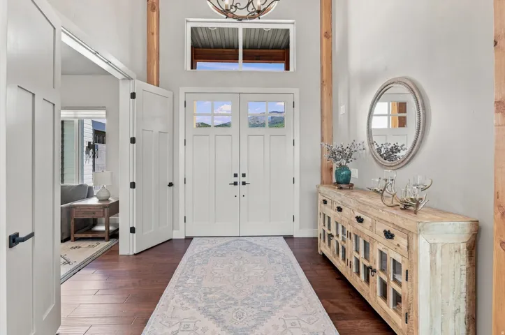 Double entry doors with glass panes, wood-finish flooring, a decorative transom window, and prominent exposed wooden beams