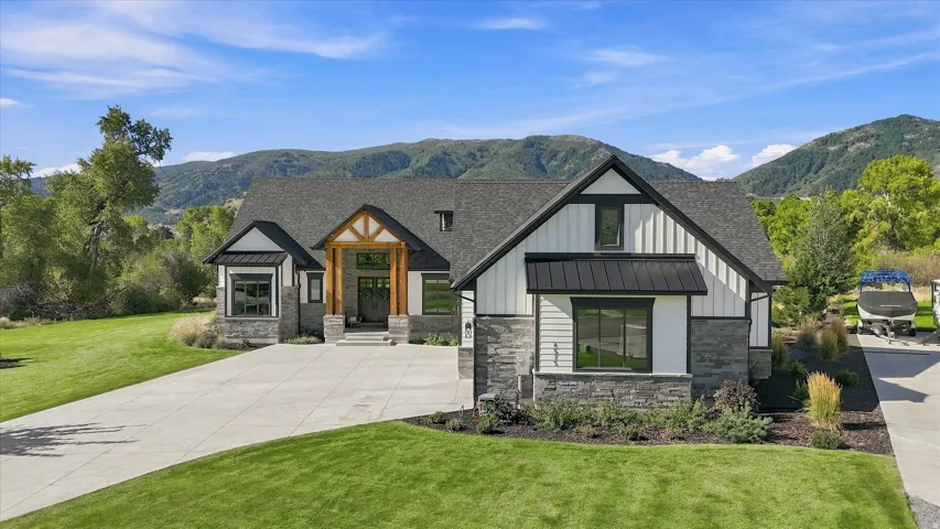 Modern craftsman-style exterior featuring stone and vertical siding, a deep gray shingle roof, and a prominent timber-framed entry