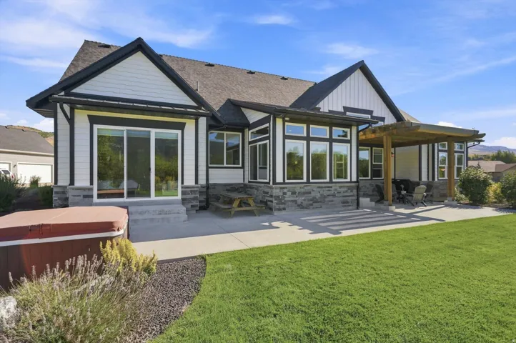 Expansive rear patio with a wood pergola, integrated landscaping, and a manicured lawn