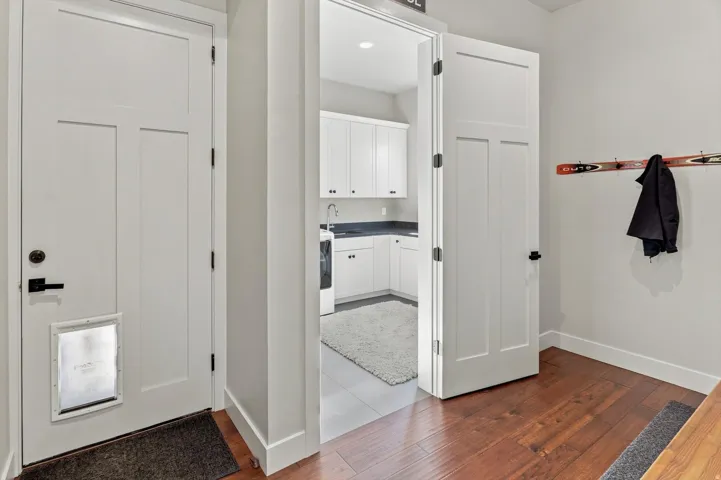 Hardwood-style flooring in entry area, white shaker-style cabinetry with dark countertops, recessed lighting, and a utility sink