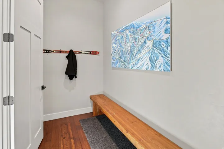 Wood-finish flooring, white paneled door with black hardware, and a wood bench