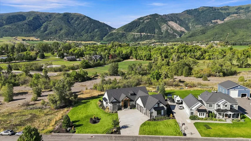 Expansive property with mountain backdrop, featuring a manicured lawn, paved driveway, and detached garage structure