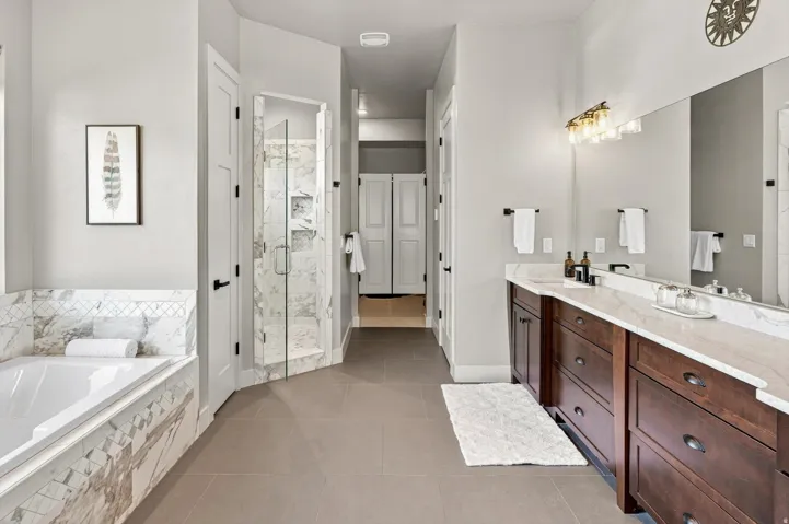 Spacious bathroom featuring a built-in soaking tub with marble surround, a glass-enclosed shower, dual vanity with wood cabinetry and stone countertops, and tile flooring