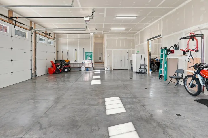 Spacious garage featuring two overhead doors with window accents, concrete flooring, and ample overhead lighting