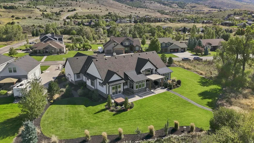 Expansive green lawn, dark shingle roofing, white siding, stone accents, and covered porch