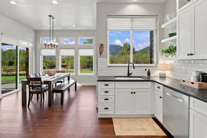 Open-concept kitchen and dining area featuring wood-finish flooring, white cabinetry, dark countertops, and a subway tile backsplash