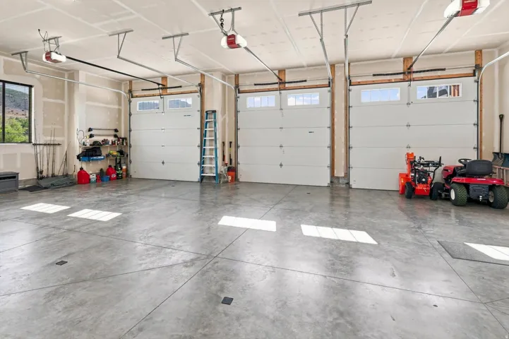 Concrete flooring, three garage doors with upper window panels, exposed wood framing, and a large window