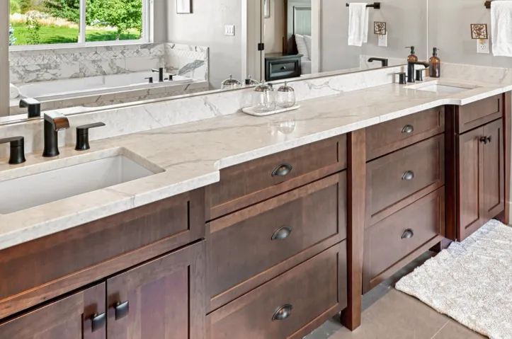 Dual undermount sinks with matte black fixtures, extensive wood-finish cabinetry, light-toned stone countertops, and a full-width mirror