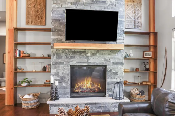 Stone-clad fireplace with a natural wood mantel, flanked by built-in shelving, featuring wood-finish flooring and exposed wood beams