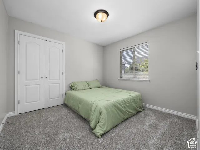 Grey carpeted flooring with white baseboards, a window with blinds, and a flush-mount ceiling light