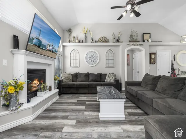 Vaulted ceiling with a ceiling fan, fireplace with a white mantle, and wood-finish flooring